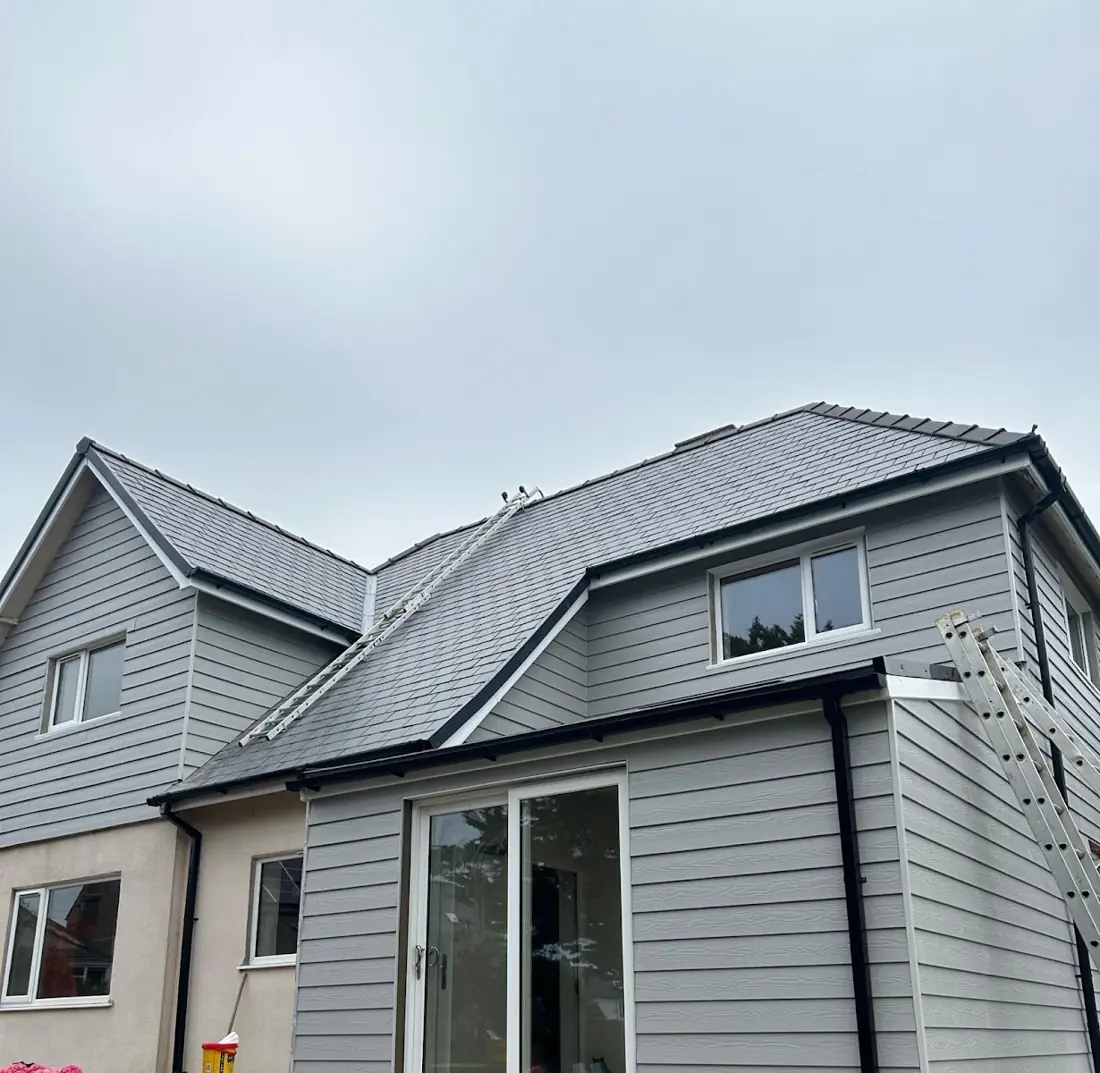 House roofed in grey slate with all the exterior walls clad, finished with black UPVC fascias and guttering. One of our jobs.