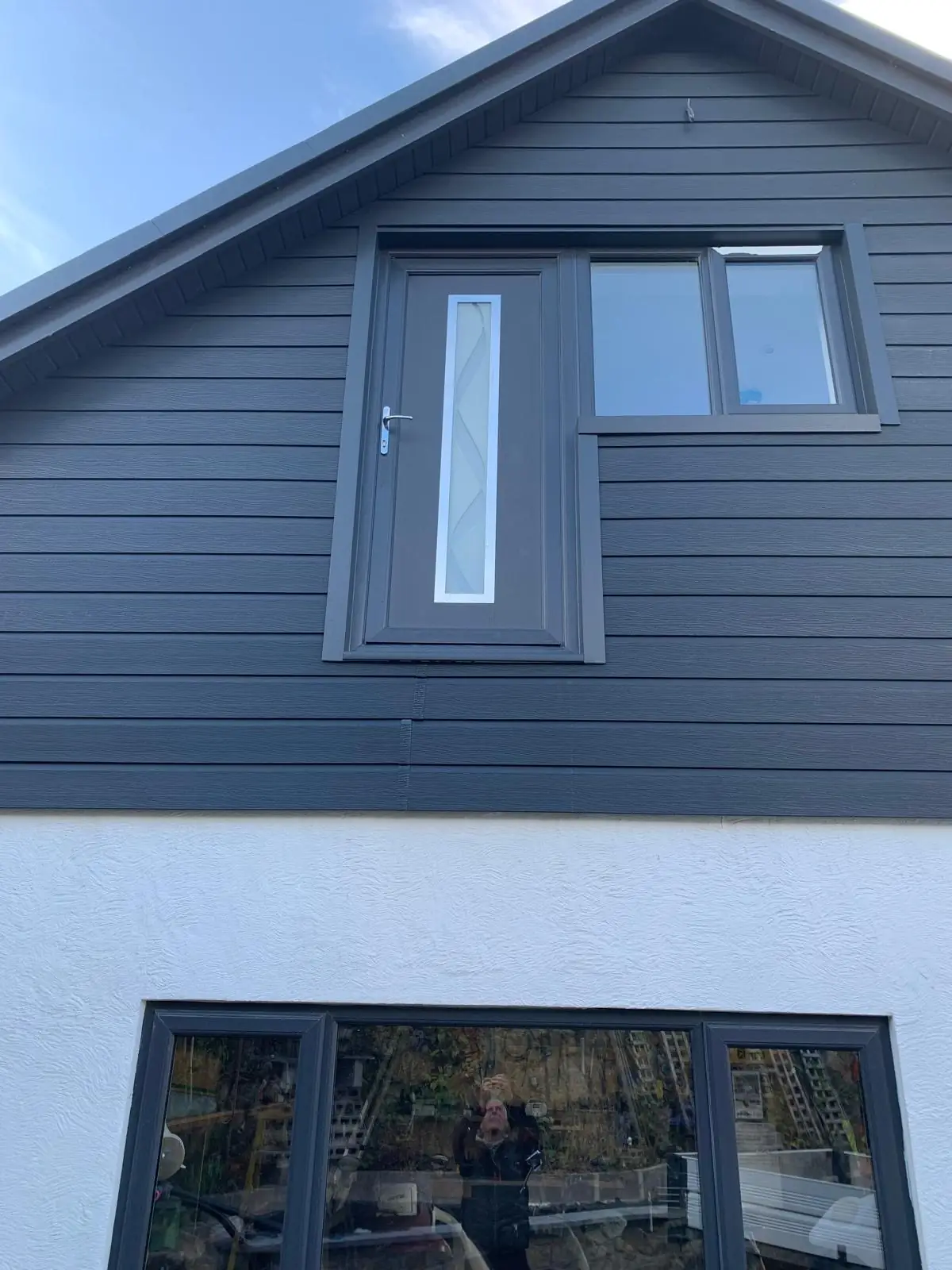 Dark grey board cladding on an upper gable above white render, with dark grey windows and door. One of our jobs.