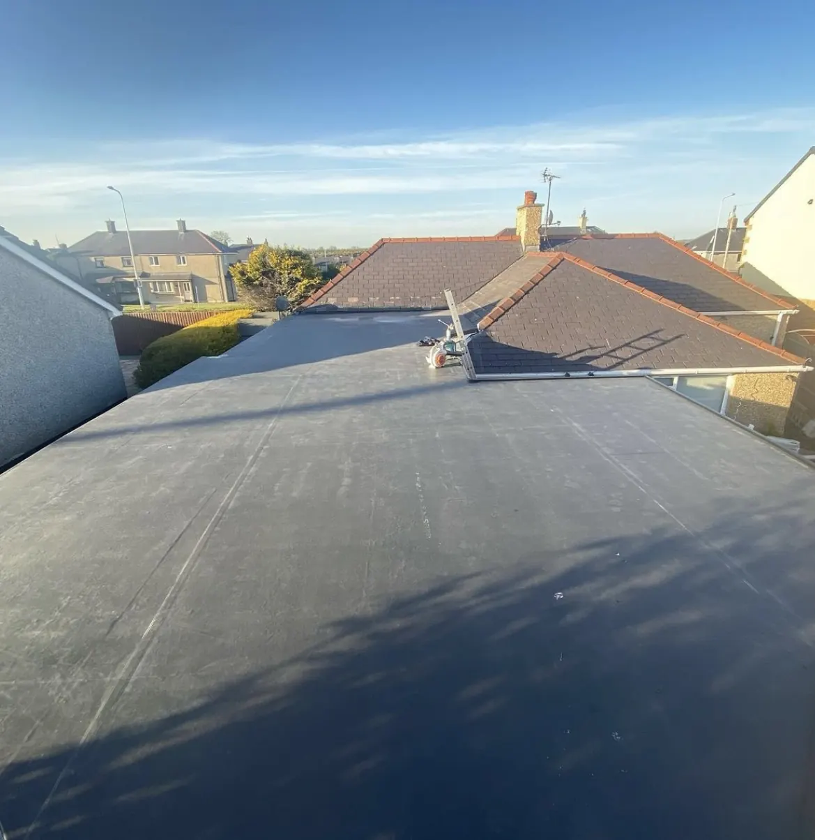 Finished black rubber flat roof, with neighbouring tiled roofs beyond. One of our jobs.