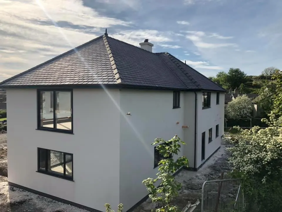 Two-storey house rendered white with a hipped slate roof and dark windows. One of our jobs.